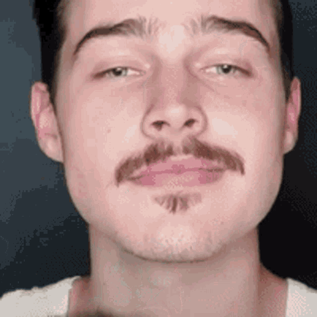 a close up of a man 's face with a mustache and a white shirt .