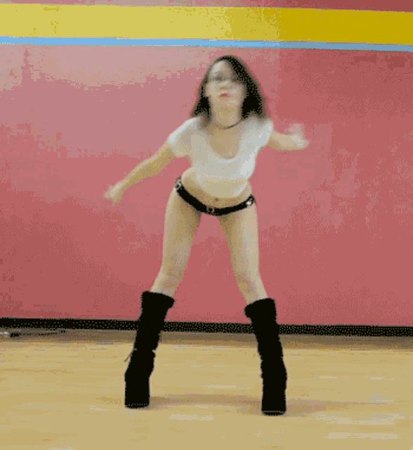 a woman in a white top and black shorts is dancing on a wooden floor