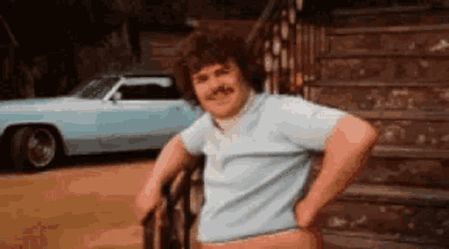 a man with a mustache is standing in front of a car