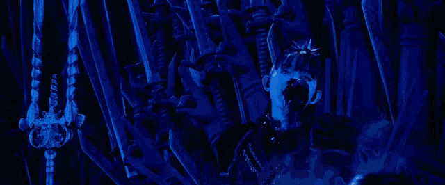 a woman with spikes on her head is sitting on a throne in a dark room with a blue background .