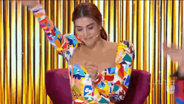a woman in a colorful dress is sitting in a chair with her arms outstretched .