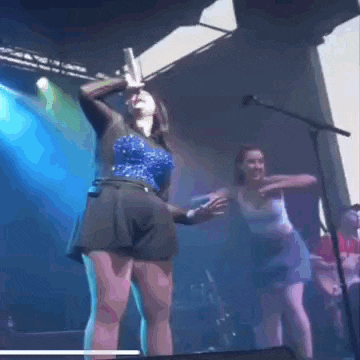 a woman is singing into a microphone on a stage while another woman is dancing behind her .