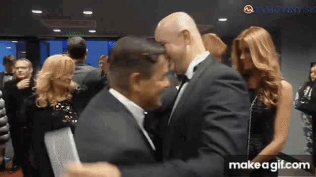 a man in a tuxedo is hugging another man in a crowd of people
