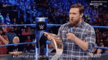 a man in a plaid shirt is talking into a microphone while holding a trophy .