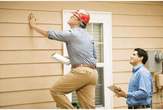 a man wearing a hard hat is standing on a ladder looking at a wall