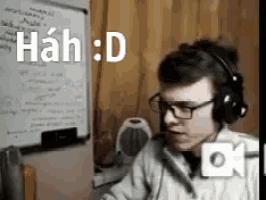 a man wearing headphones and glasses is sitting at a desk in front of a whiteboard .