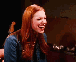 a woman with red hair is laughing while sitting in a chair