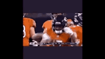 a group of football players in orange uniforms are standing around each other .