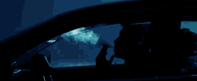 a person smoking a cigarette in a car with a blue background
