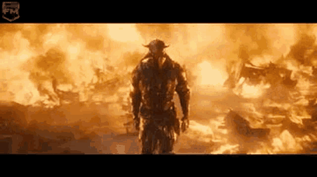 a man in a helmet is standing in front of a large fire .