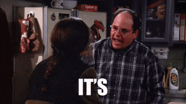 a man in a plaid shirt says it 's while talking to a woman in a kitchen