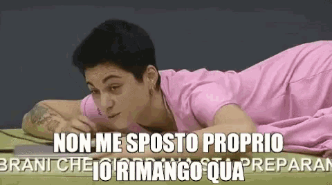 a woman in a pink shirt is laying on a bed with the words non me posto proprio written on the bottom .