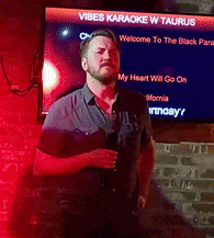 a man stands in front of a screen that says vibes karaoke w taurus on it