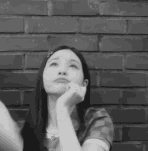 a woman is sitting in front of a brick wall with her hand on her chin .