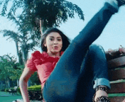 a woman in a red shirt and jeans is sitting on a bench with her leg up .