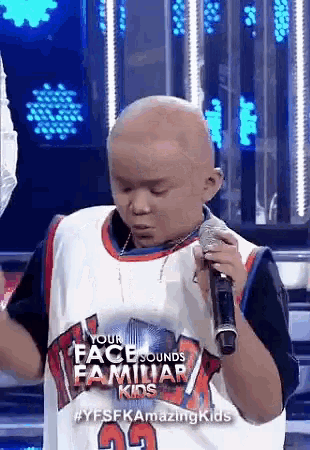 a young boy with a bald head is singing into a microphone on a stage