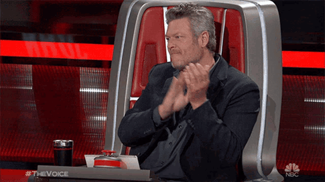 a man applauds while sitting in a chair that says nbc