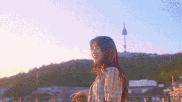 a woman is standing on a balcony overlooking a city with a tower in the background at sunset .
