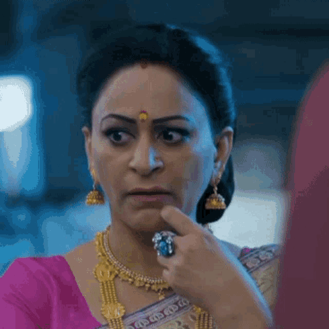 a woman wearing a pink saree and gold jewelry holds a ring in her hand