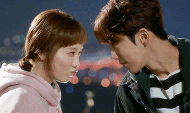 a man and a woman are looking at each other . the woman is wearing a pink hoodie .