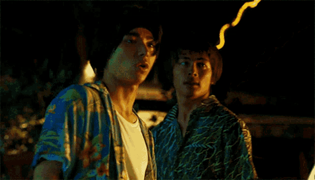 a man in a blue shirt is standing next to another man in a white shirt in the dark .