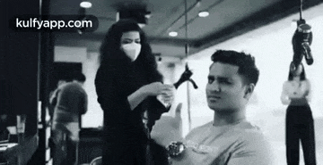 a man is getting his hair cut by a woman wearing a face mask .