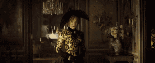 a woman wearing a black hat and gloves is standing in a dark room