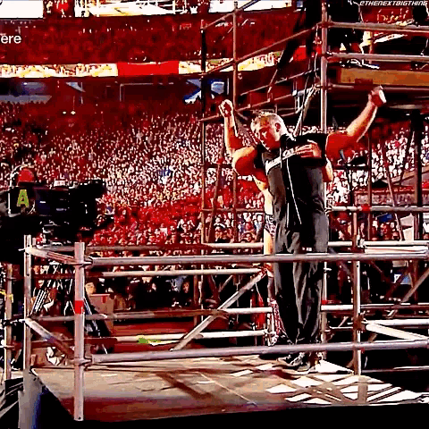 a man is standing in a ring with his arms in the air while a crowd watches .