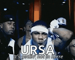 a group of people are standing around a man wearing a headband with the word ursa on it .