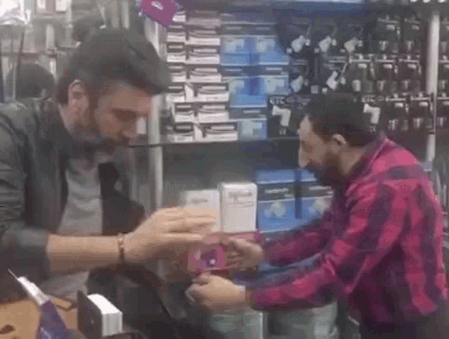 two men are standing next to each other in a store . one of the men is wearing a red and black plaid shirt .
