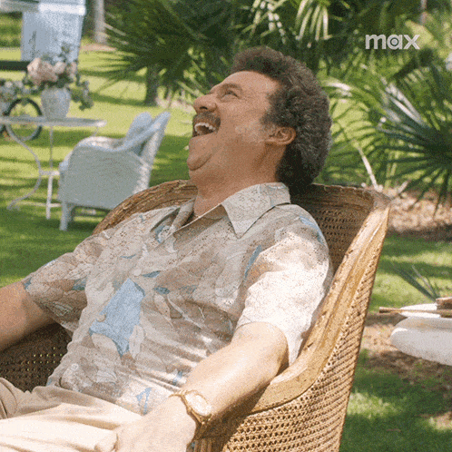 a man is sitting in a wicker chair laughing and the word max is on the bottom right