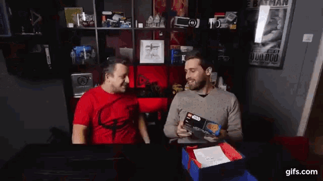 two men are sitting at a table holding a lego star wars set
