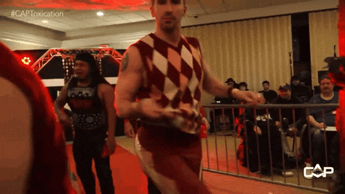 a man in a red and white checkered shirt walks down a red carpet in front of a crowd with the caption #captoxicitation