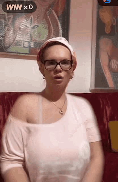 a woman wearing glasses and a scarf is sitting on a red couch with a win x 0 sticker above her head