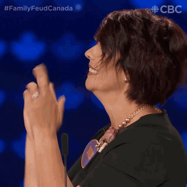 a woman in a black shirt is clapping her hands in front of a microphone with the hashtag familyfeud canada on the bottom
