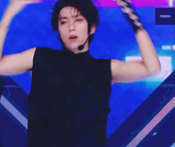 a young man is wearing a black sleeveless shirt and a microphone while dancing on a stage .