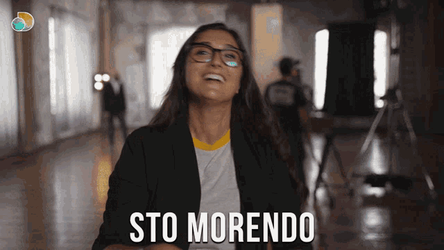 a woman wearing glasses and a black jacket is laughing and sto morendo is written below her