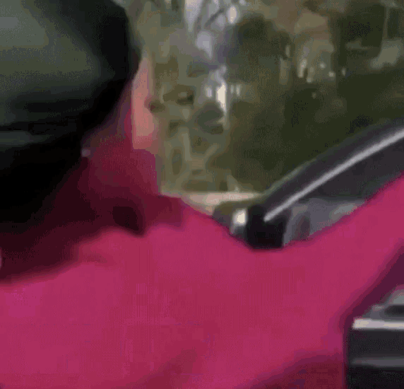 a woman in a red coat is driving a car while wearing a black hat .