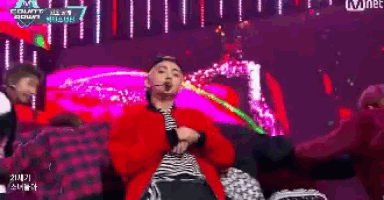 a man in a red jacket is dancing on a stage with a mnet logo in the background