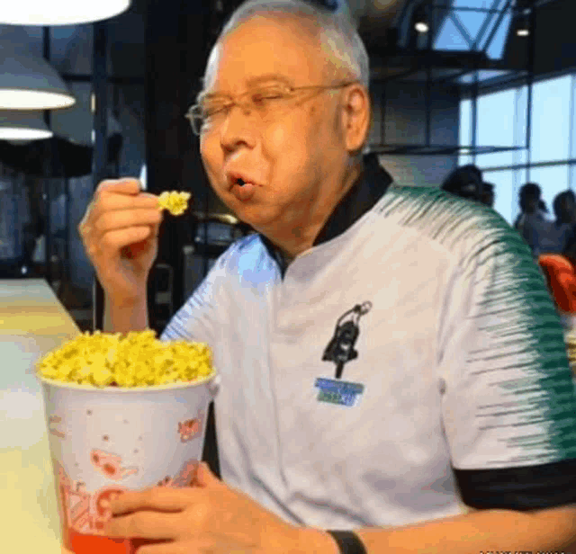 an elderly man is eating popcorn from a bucket