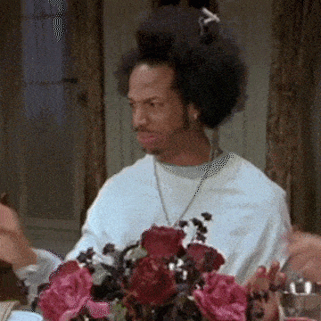 a man with an afro is sitting at a table with a vase of pink roses