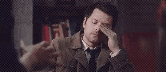 a man in a trench coat and tie is rubbing his face .