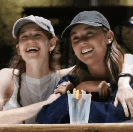 two young women are sitting at a table laughing and hugging .