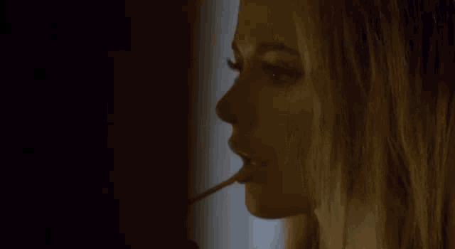 a woman is applying lip gloss with a stick in her mouth .
