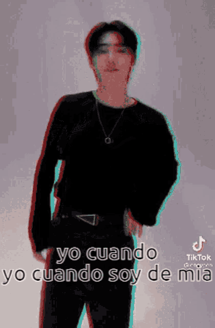 a man in a black shirt and black pants is standing in front of a wall with a purple background .
