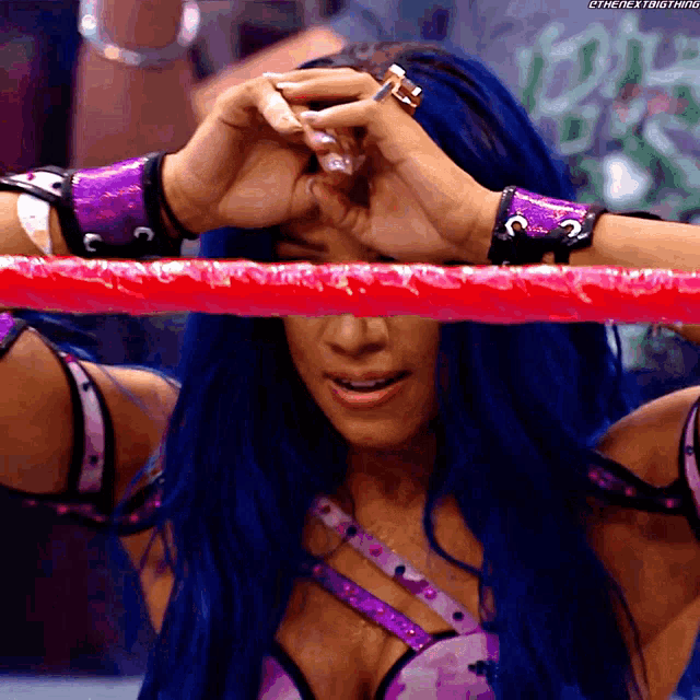 a woman with blue hair is standing in a wrestling ring with a red rope