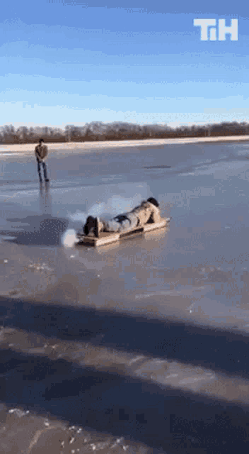 a person is laying on a sled on a frozen lake with the letters th visible in the background