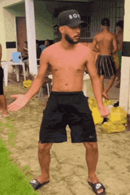 a shirtless man wearing a boy hat and black shorts stands in front of a group of people