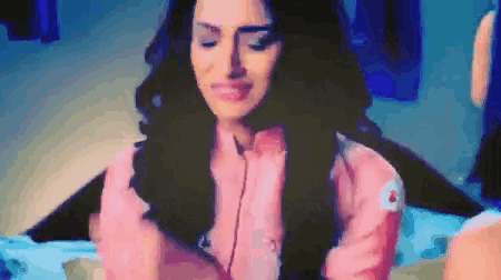 a woman in a pink shirt is sitting on a bed with her eyes closed and smiling .