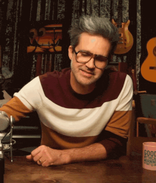 a man wearing glasses sits at a table with a cup that says good mythical morning on it